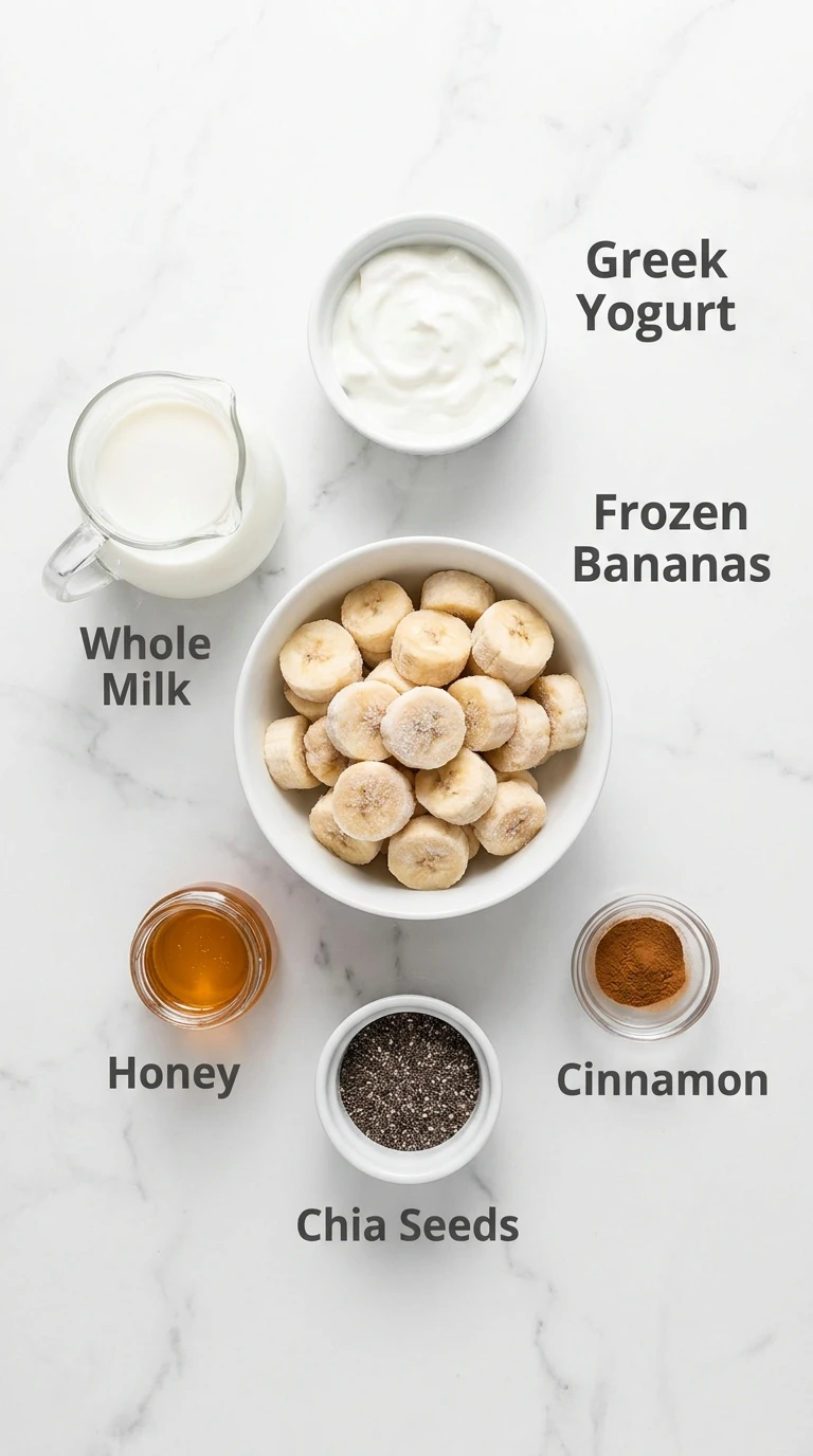 Flat-lay of Banana Smoothie recipe ingredients on marble: frozen bananas, yogurt, milk, honey, chia seeds, and cinnamon.