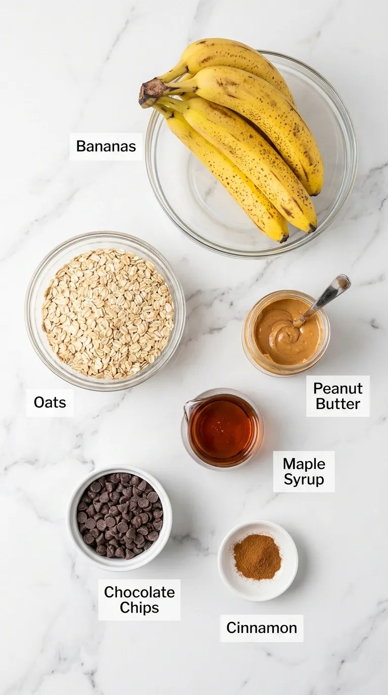 Ingredients for a healthy banana oatmeal bars recipe, labeled and arranged neatly on a white marble counter.